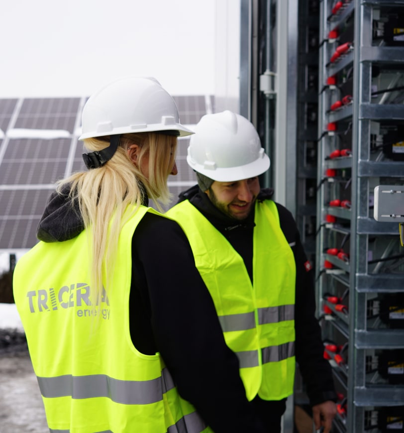 Zwei Mitarbeiter:innen mit gelben Warnwesten schauen in das Innere eines Containers mit Racks und Speichermodulen.